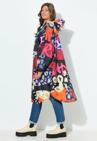 Femme portant un imperméable à capuche coloré et à motifs, un jean bleu retroussé et des bottes Chelsea à plateforme beige, marchant de côté en souriant.