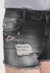 Pantalones cortos de mezclilla negra con acabado desgastado, dobladillo deshilachado y un parche con efecto desgastado. Presentan bordados en rosa y dorado de planetas y estrellas en el bolsillo.