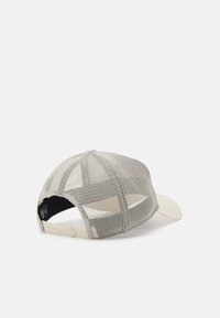 Gorra con frente beige y parte trasera de malla, forma estructurada, visera curva y cierre a presión ajustable en la parte trasera para un ajuste personalizable.