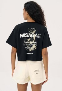 Zwarte cropped t-shirt met een witte grafische print en tekst op de achterkant. Gecombineerd met lichtgekleurde shorts met een rafelrand en achterzakken.