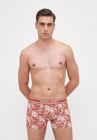 Boxer in una fantasia floreale, realizzati con un tessuto rosso ruggine e fiori bianchi, con una cintura a contrasto e logo del brand.
