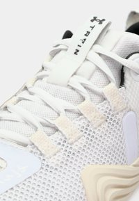 Weiße Sportschuhe verfügen über ein Mesh-Obermaterial, strukturierte Akzente und eine gepolsterte Sohle. Zu den hervorstechenden Details gehören ein Logo und eine Zuglasche an der Zunge.