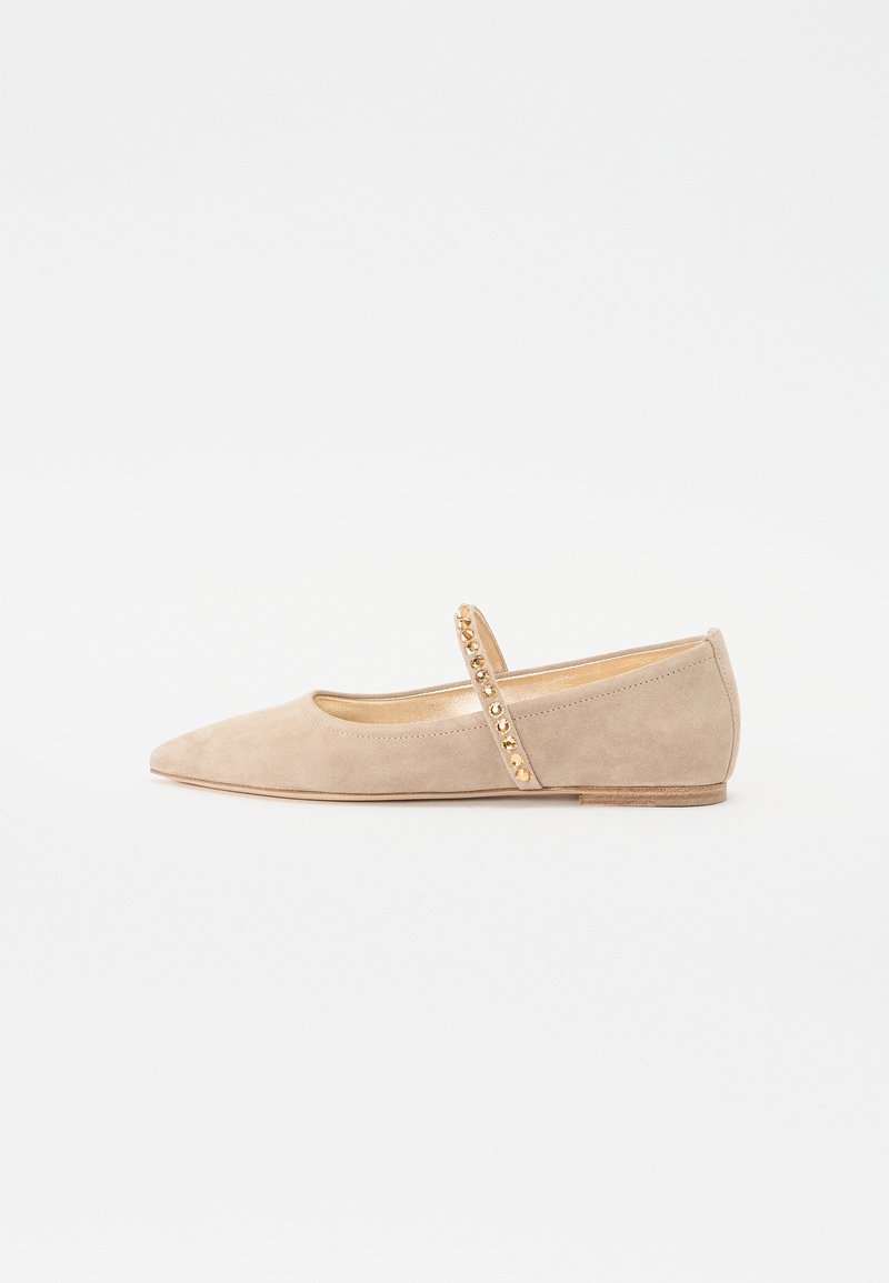 Chaussure plate en daim beige avec un bout pointu, dotée d'une sangle décorative ornée de clous dorés pour l'accent.