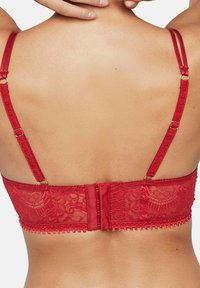 Vue arrière d'une personne portant un soutien-gorge en dentelle rouge avec des bretelles doubles réglables et une fermeture à agrafes.
