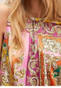 Top sin mangas colorido que presenta una mezcla de patrones en rosa, naranja y amarillo, con diseños dorados ornamentados y detalles intrincados.