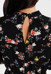 Svart blommig klänning med en nyckelhålsöppning och knäppning i ryggen som visar en kvinnas övre rygg och långt mörkt hår.