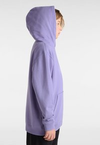 Lila Kapuzenpullover aus weichem Stoff, mit einer großen Kapuze, langen Ärmeln und einer Fronttasche, seitlich mit lässiger Passform dargestellt.