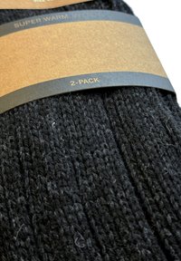 Calcetines de punto negros presentados en un paquete de 2, con un diseño texturizado y una etiqueta que indica "Super Cálido" y la información de tamaño.