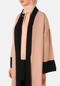 Lang, strømpejacket i blød ferskenfarve med sorte accenter og brede ærmer. Inkluderer et matchende tørklæde, der har en glat tekstur og minimal detalje.