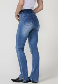 Siniset farkut, joissa on istuva leikkaus, lievää kulumista ja kontrastiväriset tikkaukset takataskuissa. Ominaisuuksiin kuuluu keskikorkea vyötärö ja leveälahkeinen helma.