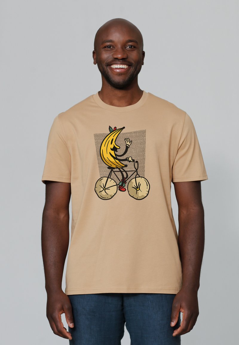 Beige t-shirt met een afbeelding van een cartoonachtige banaan die op een fiets rijdt, met een gestructureerde achtergrond en kleurrijke details.