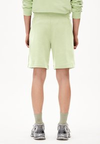 Lichtgroene katoenen shorts met een ontspannen pasvorm, voorzien van een geribbeld tailleband en omgeslagen zoom. Draag met grijze hardloopschoenen en groene sokken.