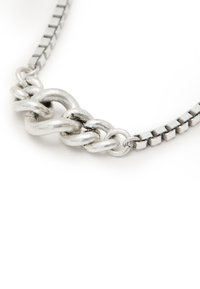 Collana in argento con catena composta da anelli circolari lisci e testurizzati interconnessi, accompagnata da una catena laterale con motivo a quadri.