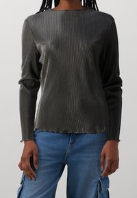 Top a maniche lunghe grigio scuro con texture a costine, caratterizzato da un collo rotondo e una silhouette aderente. Abbinato a jeans blu.