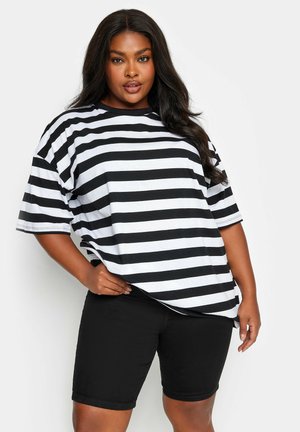Camiseta de rayas en blanco y negro de gran tamaño con mangas cortas, hecha de una tela suave, combinada con pantalones cortos negros. Estilo casual, ajuste relajado.