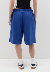 Blue cotton shorts with an elastic waistband, loose fit, and side pockets. Worn with white crew socks and blue-accented sneakers.