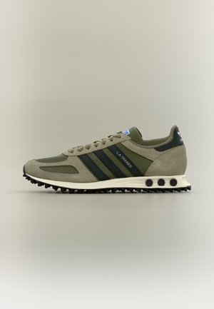 Widok z boku oliwkowo-zielonego buta sportowego Adidas LA Trainer z czarnymi paskami i białą podeszwą z czarnymi ćwiekami.