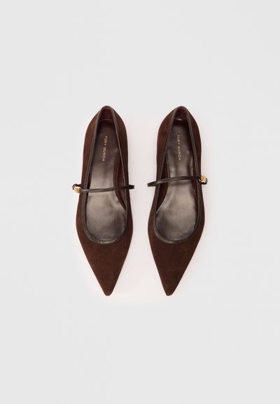 Ballerines en daim marron avec des bouts pointus, une bordure en cuir noir, et une fine sangle avec un accent décoratif en or. Doublure intérieure lisse.