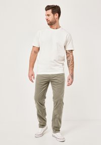 White cotton t-shirt, crew neck, worn with olive green corduroy pants and white low-top sneakers. Features arm tattoos and a relaxed fit.