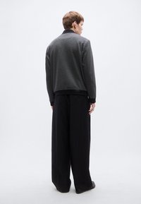 Γκρι πλεκτό πουλόβερ με μαύρο γιακά, συνδυασμένο με φαρδιά μαύρη παντελόνια. Το ντύσιμο παρουσιάζει υφασμάτινη υφή και χαλαρή σιλουέτα.