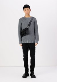 Hallus halli kudumi, millel on sooniline tekstuur, mustad cargo-püksid ja massiivsed mustad saapad. Väike ristiõla kott tekstuuriga viimistlusega.