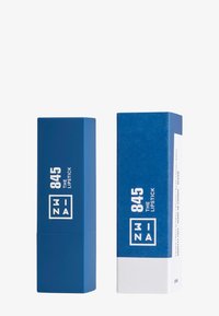 Mörkblå rektangulär läppstift-tub bredvid matchande ytterförpackning. Har vit text med produktnamn och detaljer på båda objekten.