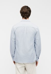 Πουκάμισο με ρίγες σε ανοιχτό μπλε και λευκό, με πίσω τμήμα γιακά, μακριά μανίκια και λεπτομέρειες με κουμπιά στα μανίκια. Βαμβακερό υλικό, άνετη εφαρμογή.