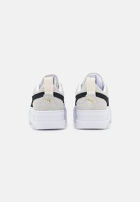Sneaker bianche con una suola spessa bianca, accenti in suede grigio, striscia di tessuto nera e dettaglio in oro sul tallone. Tallone rinforzato per supporto.