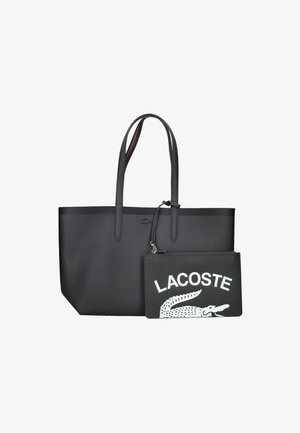 Bolsa tote negra con textura suave, dos asas largas y un bolsillo negro desmontable que presenta el texto y logotipo en blanco de "LACOSTE".