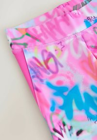 Leggings roses avec un motif inspiré du graffiti dans des couleurs vives, fabriqués en matériau lisse et extensible, avec une taille plate et des détails de couture.