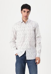 Hvit langermet skjorte med svarte håndskrevne tekstmønstre. Knappeoppgave design med krage, kombinert med blå jeans.