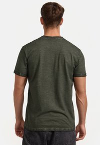 Dunkelgrünes T-Shirt mit kurzen Ärmeln aus leichtem, strukturiertem Stoff und Rundhalsausschnitt. Das Shirt hat eine lockere Passform und aufgerollte Ärmelabschlüsse.