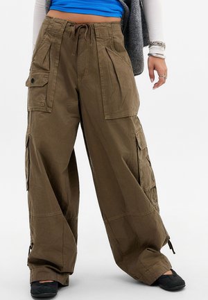 Pantalon cargo marron à jambes larges avec grandes poches et taille à cordon, porté avec des chaussures noires et un haut bleu visible au-dessus de la taille.