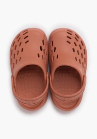 Red rubber clogs with vent holes and a flexible strap. Textured footbed with rounded nubs for grip. Lightweight and open design.
