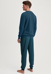 Donkerblauw langemouwtop met een ronde hals, gecombineerd met lichte pyjamabroek met een bloemenpatroon in groen en wit.
