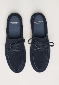 Navy suede moccasin shoes with round toe, laced closure, and contrast stitching. Interior features brand logo, “FRED MARTIN, MADE IN SPAIN.”