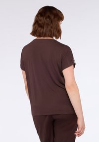Camiseta de manga corta marrón con cuello redondo y un ajuste holgado. La tela parece suave y ligera, con detalles sutiles en las mangas.