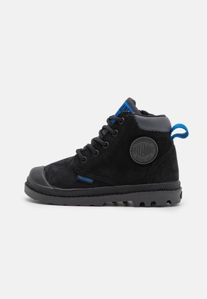 Botte montante noire Palladium avec semelle en caoutchouc, languette en tissu bleu, patch logo rond, et fermeture avant à lacets.