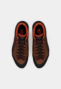 Παπούτσια πεζοπορίας σε καφέ και μαύρο χρώμα, με πορτοκαλί λεπτομέρειες, υφασμένη επάνω επιφάνεια, ενισχυμένη μύτη και μαύρα κορδόνια με κόκκινες ραφές.