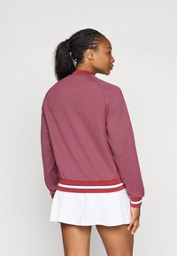 Bordo bomberio striukė su raukšlėtu apykakle ir rankovėmis, su balta ir raudona dryžuota apatine dalimi. Audinys su tekstūra, laisvas kirpimas.