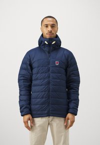 Námornícky puffový kabát s horizontálnym prešívaním, vysokým golierom a zipsom. Obsahuje nášivku s logom na ľavej hrudi a žlté akcentované gombíky.
