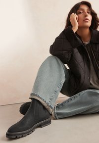 Schwarze Stiefeletten aus strukturiertem Material mit elastischen Seitenteilen und einer robusten Sohle, kombiniert mit hellblauem, locker sitzendem Denim.