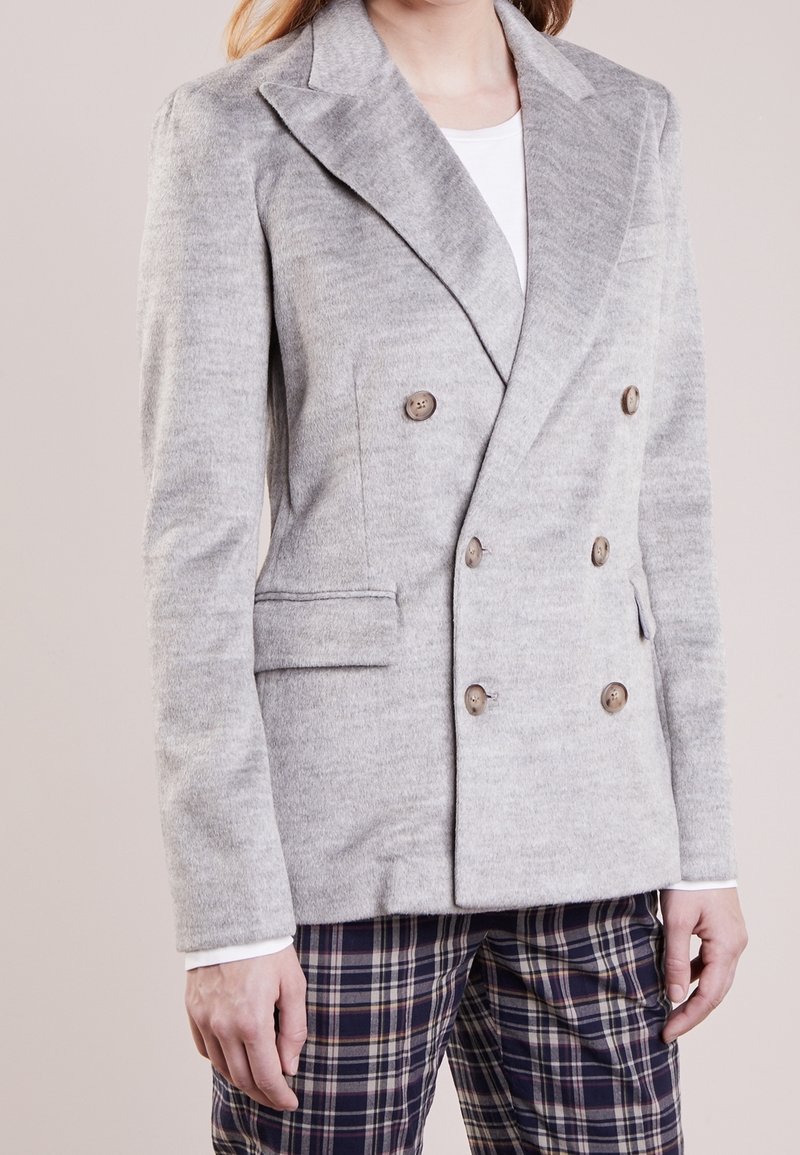 Gray double-breasted blazer with pronounced lapels, textured fabric, and two front pockets, paired with plaid patterned trousers.