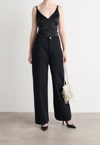 Svart satin topp med V-ringning, kombinerad med högmidjade vida svarta jeans med små detaljer, och en fransad metallväska.