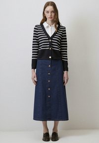 Marine gestreepte cardigan met gouden knopen, gecombineerd met een lange denim rok met knopen aan de voorkant en een rechte snit. Bruine schoenen maken de outfit compleet.