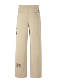 Pantalon beige à jambes larges avec poches fendues à l'arrière et texte noir "Don Ed Hardy designs" sur la partie inférieure de la jambe gauche.