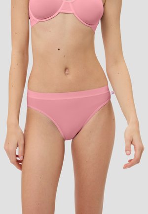 Frau trägt passenden hellrosa BH und Bikini-Unterwäsche vor einem einfarbigen hellgrauen Hintergrund.