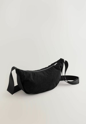 Riñonera de pana negra con cierre de cremallera suave, correa de tela ajustable y superficie suave y texturada. Diseño simple y curvado.