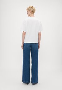 Hvit kortermet T-skjorte kombinert med høy midje og vid ben blå denimbukser. Buksene har klassiske lommer og råkant.