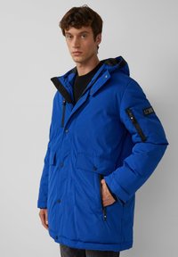 Blaue isolierte Parka mit Kapuze, ausgestattet mit einem Frontreißverschluss, Druckknopfverschluss, Seitentaschen und einer mit Reißverschluss versehenen Ärmeltasche mit Akzentdetails.